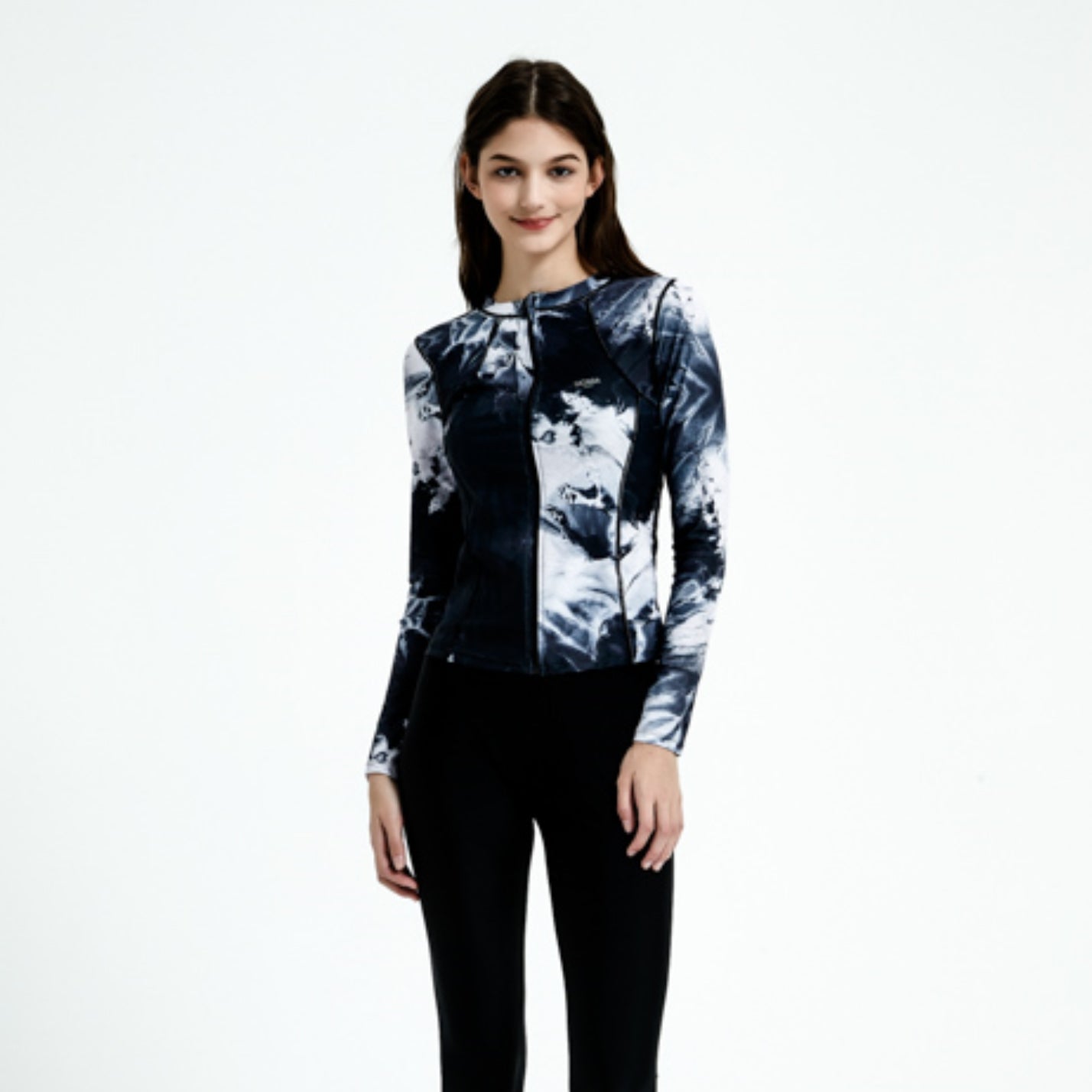 在白色背景下,一位棕色長髮的女性露出柔和的微笑,她身穿黑色 4 件套裝運動泳衣 <22121651>,上衣為黑白圖案拉鍊上衣,下身穿黑色褲子。.