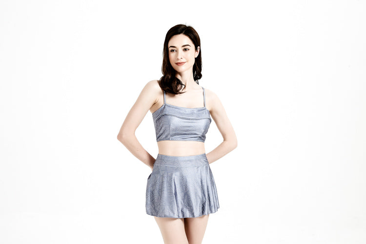 一位深色長髮的女性背著手,站在白色背景中,臉上帶著柔和的微笑。她穿著中灰色-MIX&MATCH泳衣上身 <23551488>,為她的造型增添時髦感。.