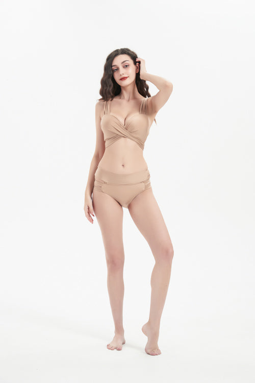 一位深色長髮的女性在白色背景下赤腳擺姿勢,身著杏色搭帶MIX&MATCH泳衣下身 <24151601>-米色裹身式比基尼下身,搭配高腰設計的修飾身材。一隻手摸著她的頭。.