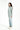 一名女子側身站立，身穿綠色冰感外套 <20121356-30>、淺藍色牛仔褲和白色運動鞋，背景為純白背景。.