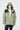 一個人面向前方站立，穿著杏色 2合1撥水防風外套 <20621678-12>，外罩白色 T恤，在素雅的淺色背景下，突顯都會休閒風格。.