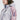 一個人穿著 2 合 1 撥水防風外套 <20621685-106>，一件有拉鍊、胸前口袋、袖子標誌的粉紅-紫-白色圖案連帽外套；他們的臉只能看到一部分。.