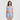一位棕色長髮的女性站在白色背景中，身穿天藍色 4 件套裝運動泳衣 <21211824> - 一件藍白相間的夏季運動服，搭配上衣和短褲，中性地凝望著鏡頭。.