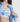 棕色長髮的女子打開藍白拼接外套，露出天藍色 4 件套裝運動泳衣 <21211824> 的熱帶藍綠色調。純白的背景突顯出毫不費力的夏日運動服風格。.