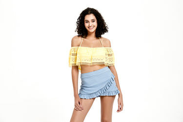 一名捲髮女子身穿黃色露肩 crop top 和藍色高腰裙 MIX&MATCH泳衣下身 <24091593>，站在純白背景下微笑。.