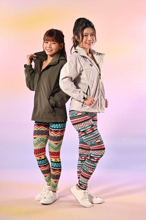 兩位女士面帶微笑，背靠背站著，各自穿著色彩繽紛的圖案緊身褲、白色運動鞋和拉鍊式外套，背景是粉彩漸層色。.