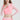 粉紅色短腰分體套裝運動泳衣 <21231787> 中的女性微笑著，一隻手放在胸前，另一隻手放在臀部，在純白背景下展現出時尚的防曬泳衣造型。.